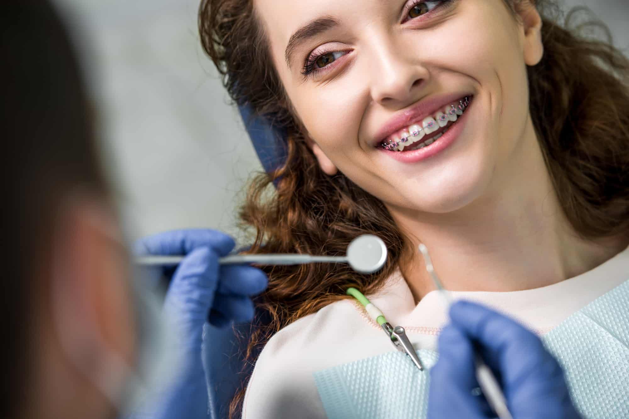 Close up of cheerful woman in braces during examination of teeth near dentist